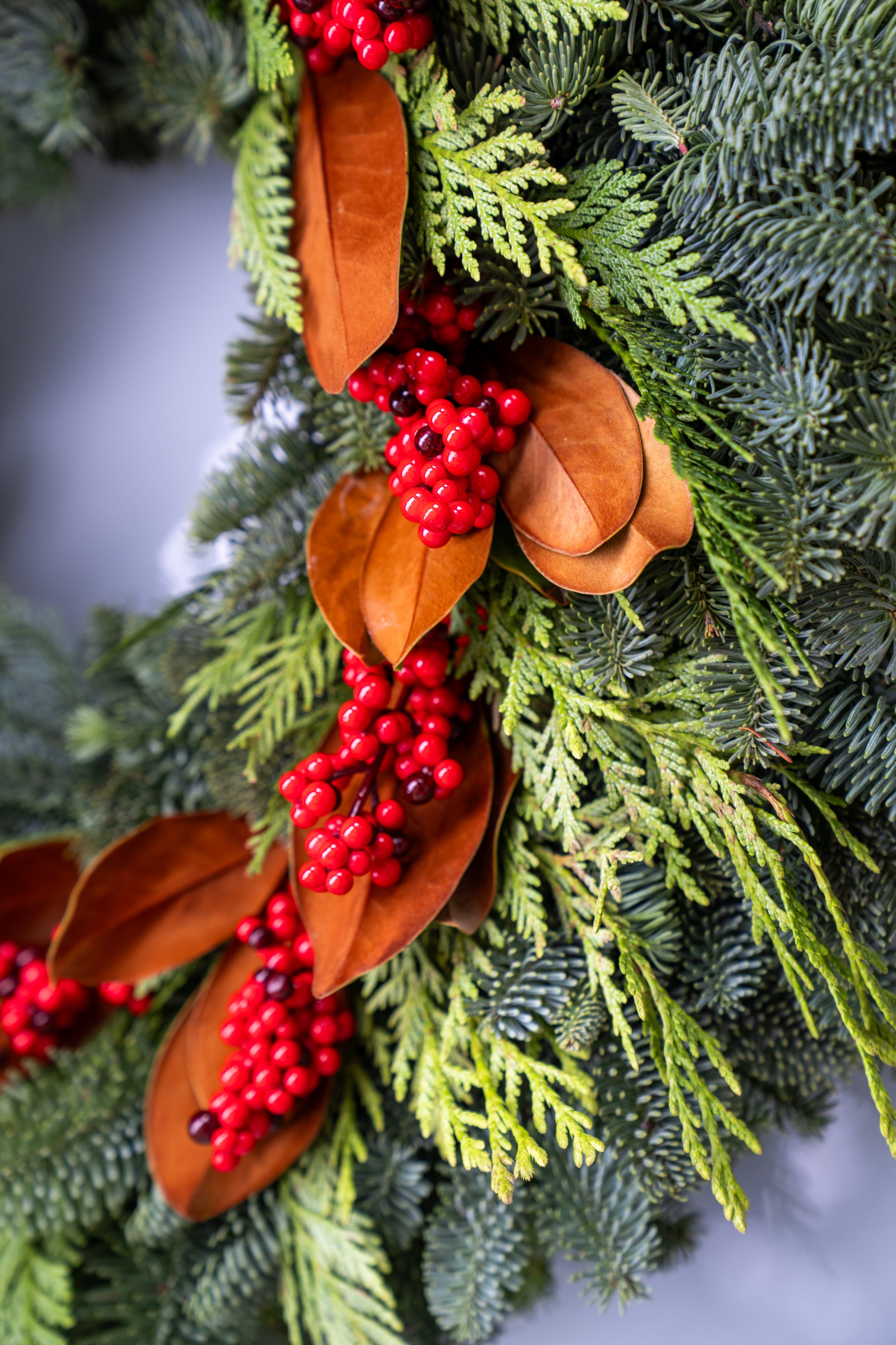 Close-up of a Christmas wreath with greenery, red berries, and brown leaves.