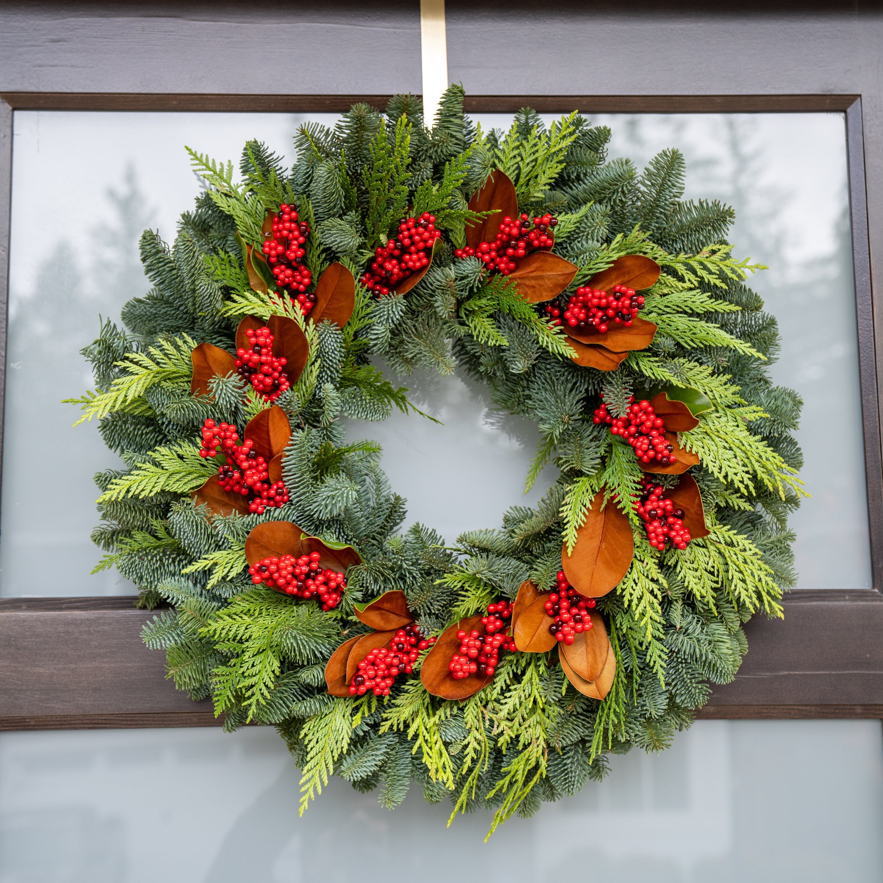 Christmas wreath with greenery, red berries, and orange leaves hanging on a door.