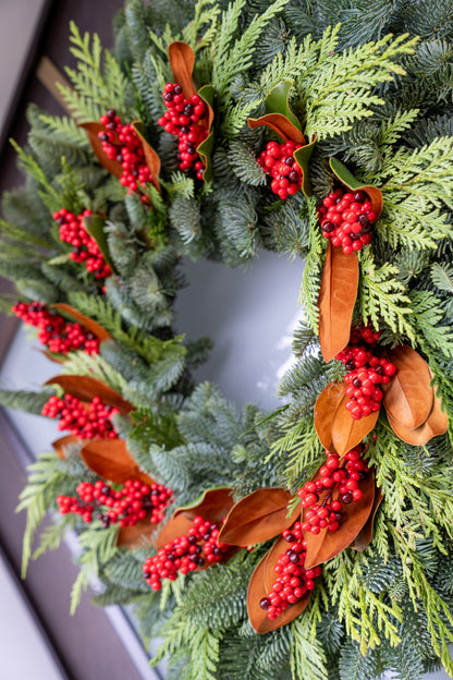 Christmas wreath with greenery, red berries, and brown ribbons on a white background