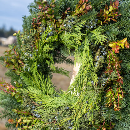 Green wreath with natural elements held by a person outdoors